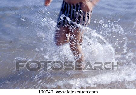 Stock Photo - Low section view of man running in water on beach . Fotosearch