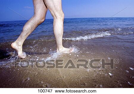 Stock Photo - Low section view of man walking in water on beach . Fotosearch