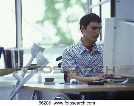 Stock Photography - Man in wheelchair using computer in office . Fotosearch