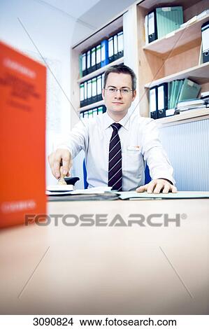 Man sitting at a desk, holding stamp in his hand, low angle view View Large Photo Image Picture - Man sitting at a desk, holding stamp in his hand, low angle view . Fotosearch