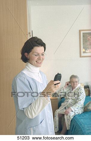 Nurse using mobile phone with patient in background View Large Photo Image Stock Image - Nurse using mobile phone with patient in background . Fotosearch