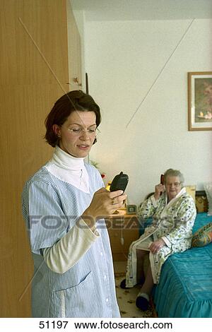 Stock Photo - Nurse using mobile phone with patient in background . Fotosearch
