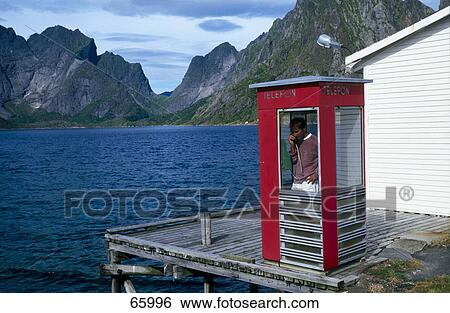 Stock Photograph - Person using the landline phone inside a telephone booth, Fjords, Norway . Fotosearch