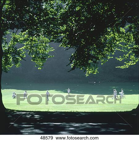 Stock Photo - Players playing cricket in park, Sussex, England . Fotosearch