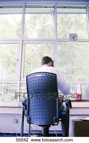 Stock Image - Rear view of businessman talking on mobile phone in office . Fotosearch