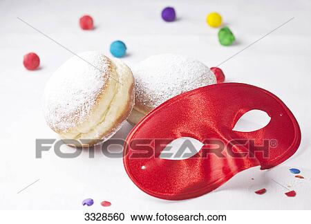 Stock Image - Red carnival mask, doughnuts and confetti, close-up . Fotosearch