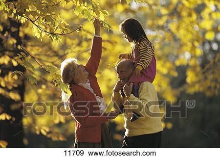 Stock Photo - Senior couple smiling with their grandchild in a park . Fotosearch
