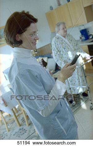 Picture - Side profile of nurse using mobile phone with patient in background . Fotosearch
