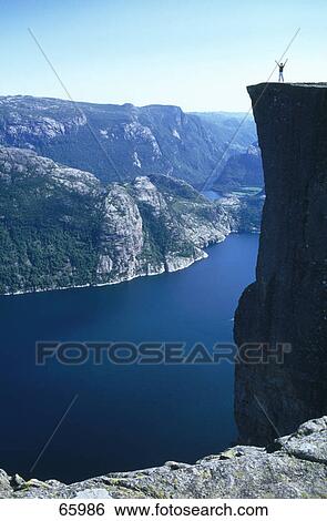 Stock Photograph - Silhouette of person standing on cliff and raising hands, Preikestolen, Rogaland, Norway . Fotosearch