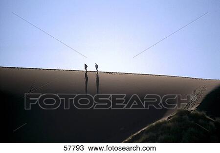 Silhouette of two people walking on sand dune View Large Photo Image Stock Image - Silhouette of two people walking on sand dune . Fotosearch