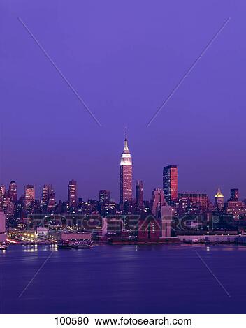 Stock Image - Skyscrapers lit up at riverbank, Empire State Building, Hudson River, New York City, New York State, USA . Fotosearch