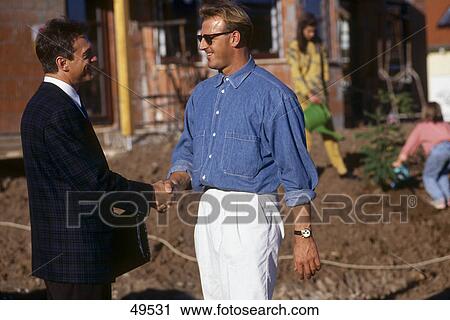 Stock Image - Two men shaking hands at construction site . Fotosearch
