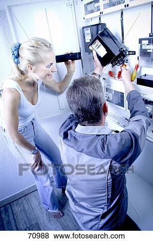 Stock Photo - Young woman showing flash light to male electrician working in house . Fotosearch