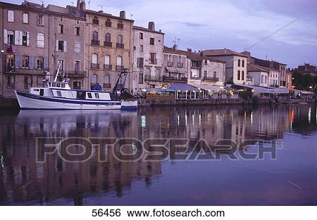 Stock Photograph - Buildings at waterfront reflected in river, Orb River, Agde, Herault, France . Fotosearch