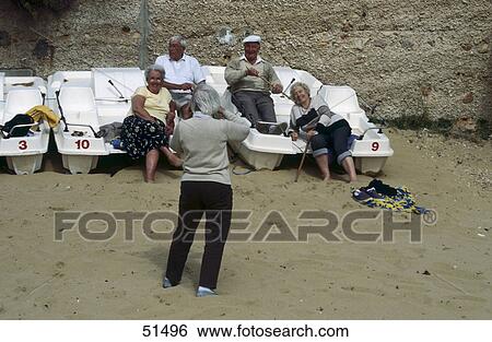 Stock Photograph - Rear view of man taking photographs of senior couple on beach, Golden Bay, Malta . Fotosearch