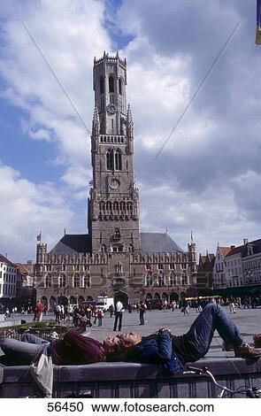 Stock Image - Two men sleeping on wall in front of clock tower, Bruges, Belgium . Fotosearch