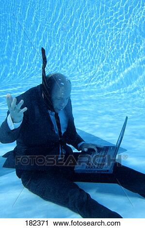 Stock Image - Businessman using laptop in swimming pool, underwater view . Fotosearch