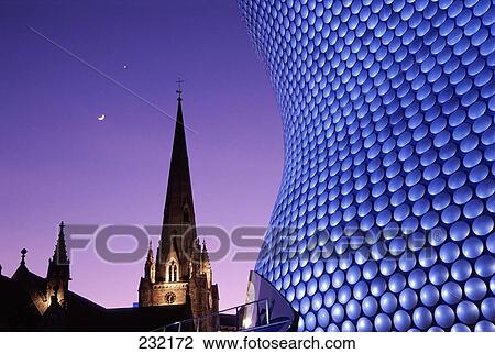 Stock Image - Close-up of building with church in background at night, Selfridges Building, St Martins Church, Birmingham, England . Fotosearch