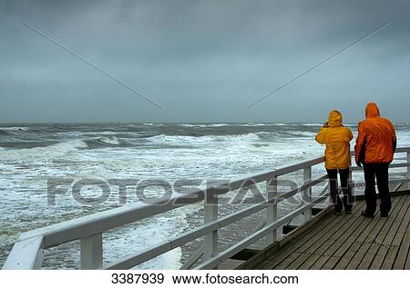 Couple on waterside promenade looking at stormy sea, rear view View Large Photo Image Stock Photo - Couple on waterside promenade looking at stormy sea, rear view . Fotosearch