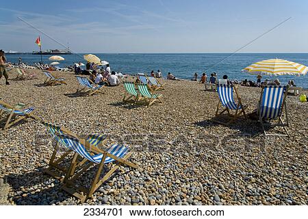 Stock Image - Deck chairs and tourists on beach, Brighton, East Sussex, England . Fotosearch