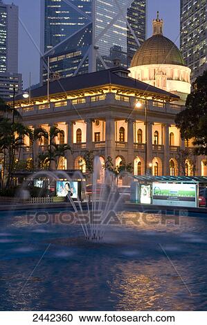 Stock Image - Fountain in front of lit up building . Fotosearch