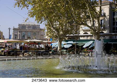 Stock Image - Fountain with market stalls in background, Place De La Comedie, Montpellier, Herault, Languedoc-Rousillon, France . Fotosearch