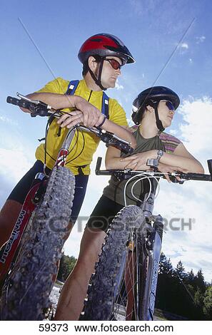 Stock Image - Low angle view of couple with bicycles . Fotosearch