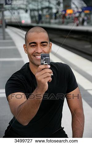 Stock Photo - Man at railway station taking a picture with his mobile phone . Fotosearch