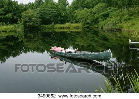 Stock Image - Man lying in a canoe on a pond, elevated view . Fotosearch