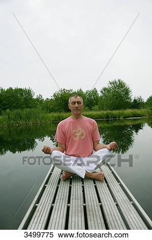 Stock Photography - Man sitting in lotus position on a jetty by a lake, front view . Fotosearch
