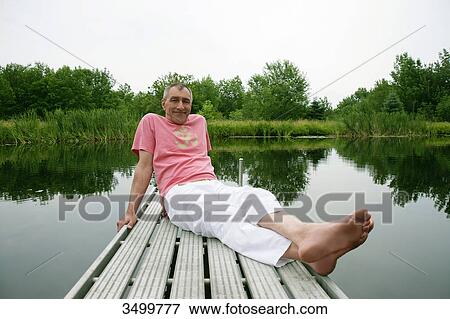 Stock Photo - Man sitting on a jetty by a lake . Fotosearch