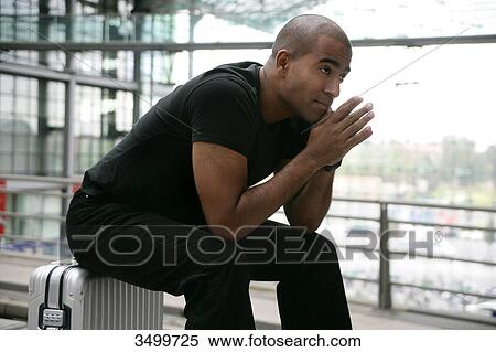 Stock Photography - Man sitting on a suitcase at railway station, low angle view . Fotosearch