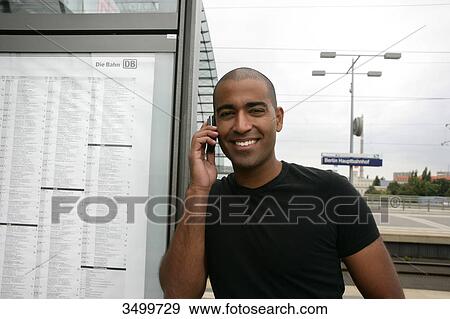 Stock Photo - Man using mobile phone at railway station, front view . Fotosearch