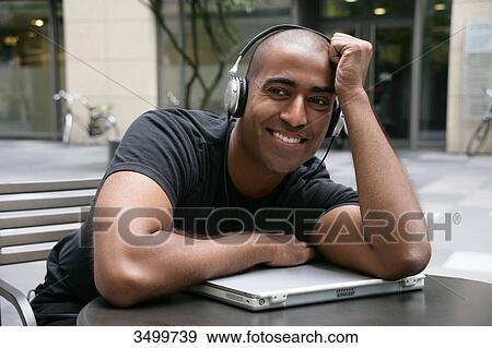 Man with headphones leaning against notebook View Large Photo Image Stock Photo - Man with headphones leaning against notebook . Fotosearch
