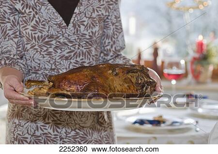 Stock Image - Mid section view of woman holding tray of roasted christmas goose . Fotosearch
