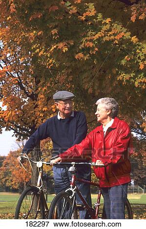 Stock Photo - Senior couple walking with bicycles in park . Fotosearch