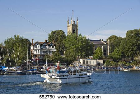 Stock Image - Tourboat in river with church in background, Thames River, Hampton Church, Hampton, London, England . Fotosearch