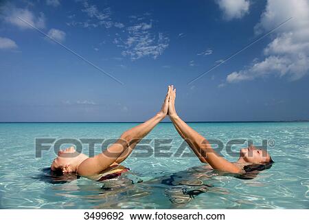 Two women in the water touching their hands and reclining, side view View Large Photo Image Stock Image - Two women in the water touching their hands and reclining, side view . Fotosearch