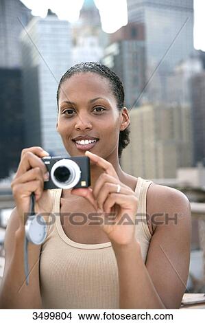 Picture - Woman holding a digital camera, skyline of New York in the background, USA . Fotosearch
