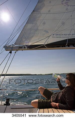 Stock Image - Woman lying on the deck of a sailing yacht and drinking water . Fotosearch