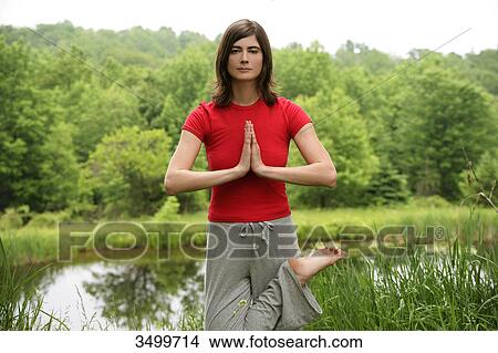 Woman practising yoga by a pond, front view View Large Photo Image Picture - Woman practising yoga by a pond, front view . Fotosearch