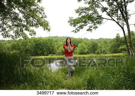 Stock Photo - Woman practising yoga by a pond, front view . Fotosearch