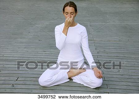 Stock Image - Woman sitting in lotus position on a deck, front view . Fotosearch