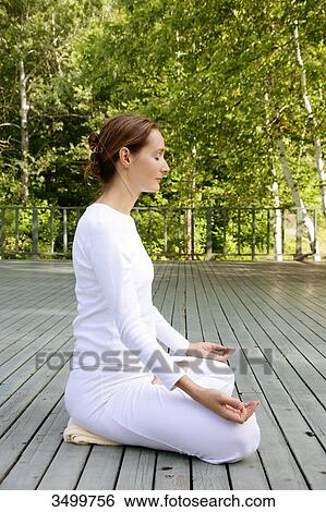 Stock Photograph - Woman sitting in lotus position on a deck, side view . Fotosearch