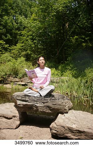 Woman sitting on a rock and holding a book View Large Photo Image Stock Image - Woman sitting on a rock and holding a book . Fotosearch