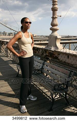 Stock Image - Woman standing on the Brooklyn Bridge with hands on her hips, New York City, USA . Fotosearch
