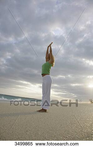 Stock Photography - Young woman practising yoga on a beach, low angle view . Fotosearch