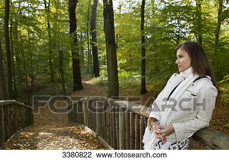 Stock Image - Young woman standing on bridge in forest . Fotosearch