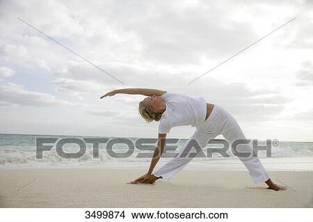 Picture - Young woman stretching on a beach, low angle view . Fotosearch