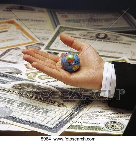Picture - Close-up of stock certificates and person's hand holding globe . Fotosearch